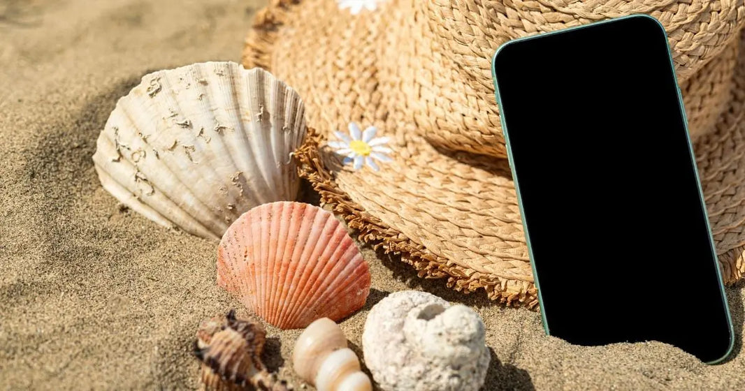 Smartphone posé dans le sable en bord de mer avec coquillages, illustration d’un nettoyage complet après les vacances d’été, conseils iTelier Lyon pour protéger et entretenir son téléphone.