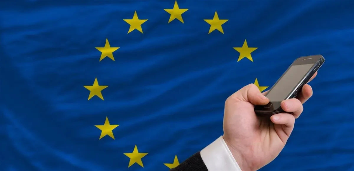Main tenant un smartphone devant le drapeau de l’Union Européenne – nouvelles réglementations 2025 facilitant la réparation et prolongeant la durée de vie des téléphones.