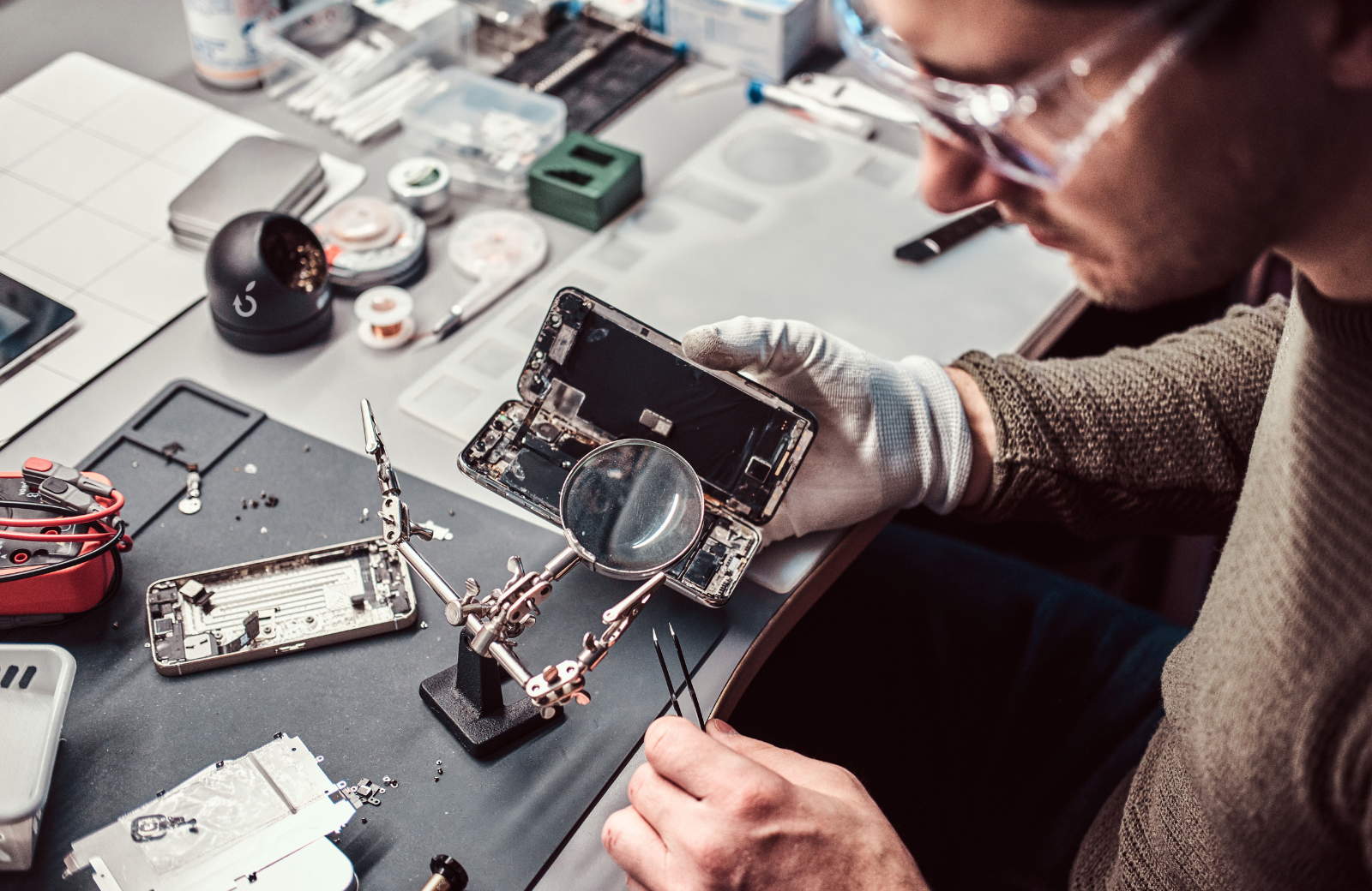 Technicien iTelier à Lyon effectuant la réparation d’un smartphone avec outils de précision et loupe, diagnostic minutieux et remplacement de composants pour garantir un service de haute qualité.